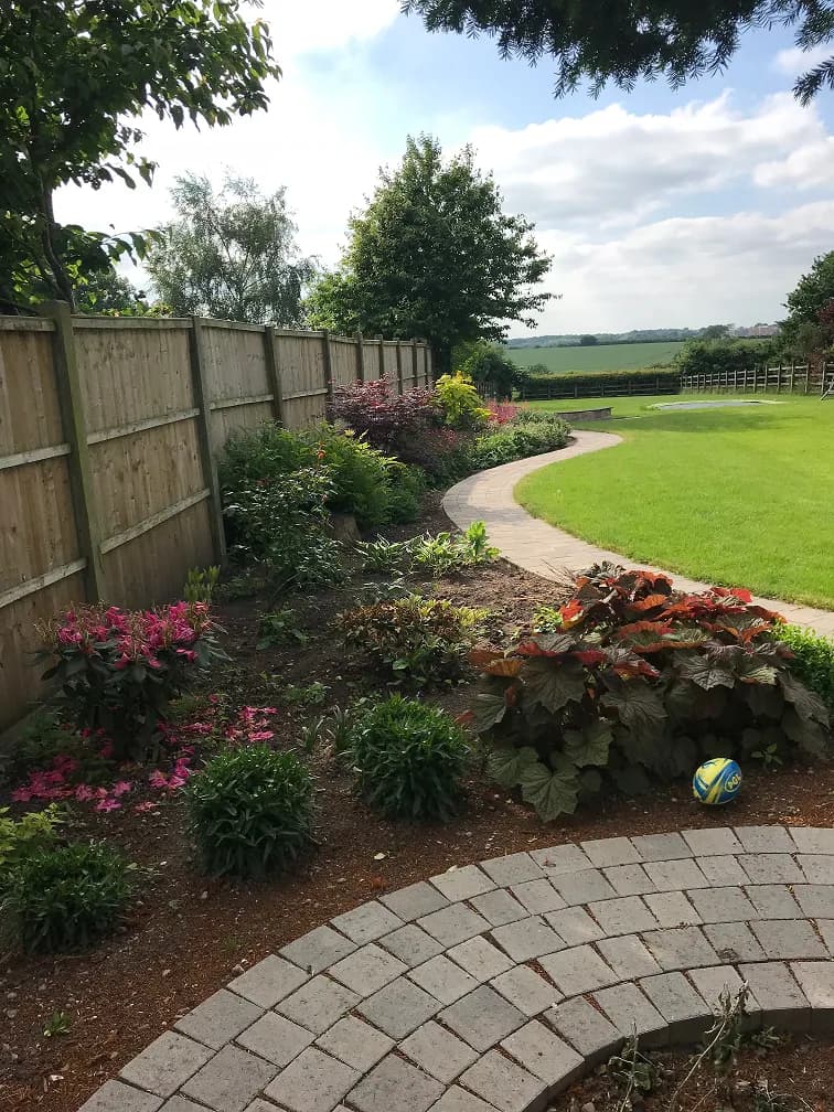 Curved garden path with landscaped flower borders, lawn, timber fencing and countryside views.