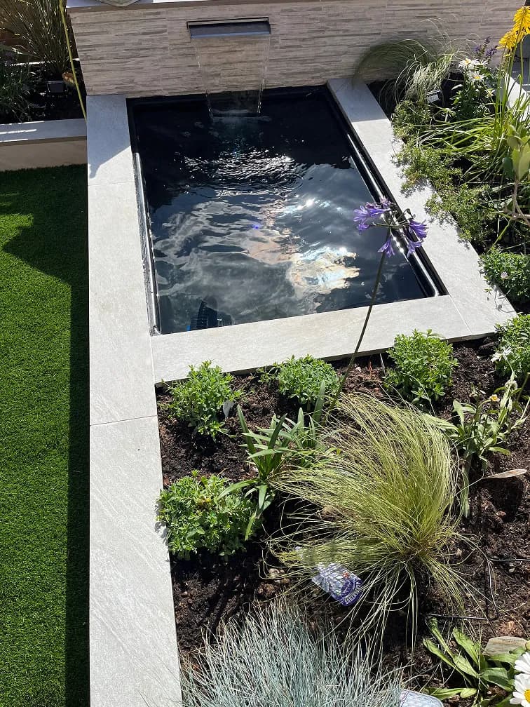 Raised garden pond with water blade feature, porcelain edging, ornamental grasses and modern planting.